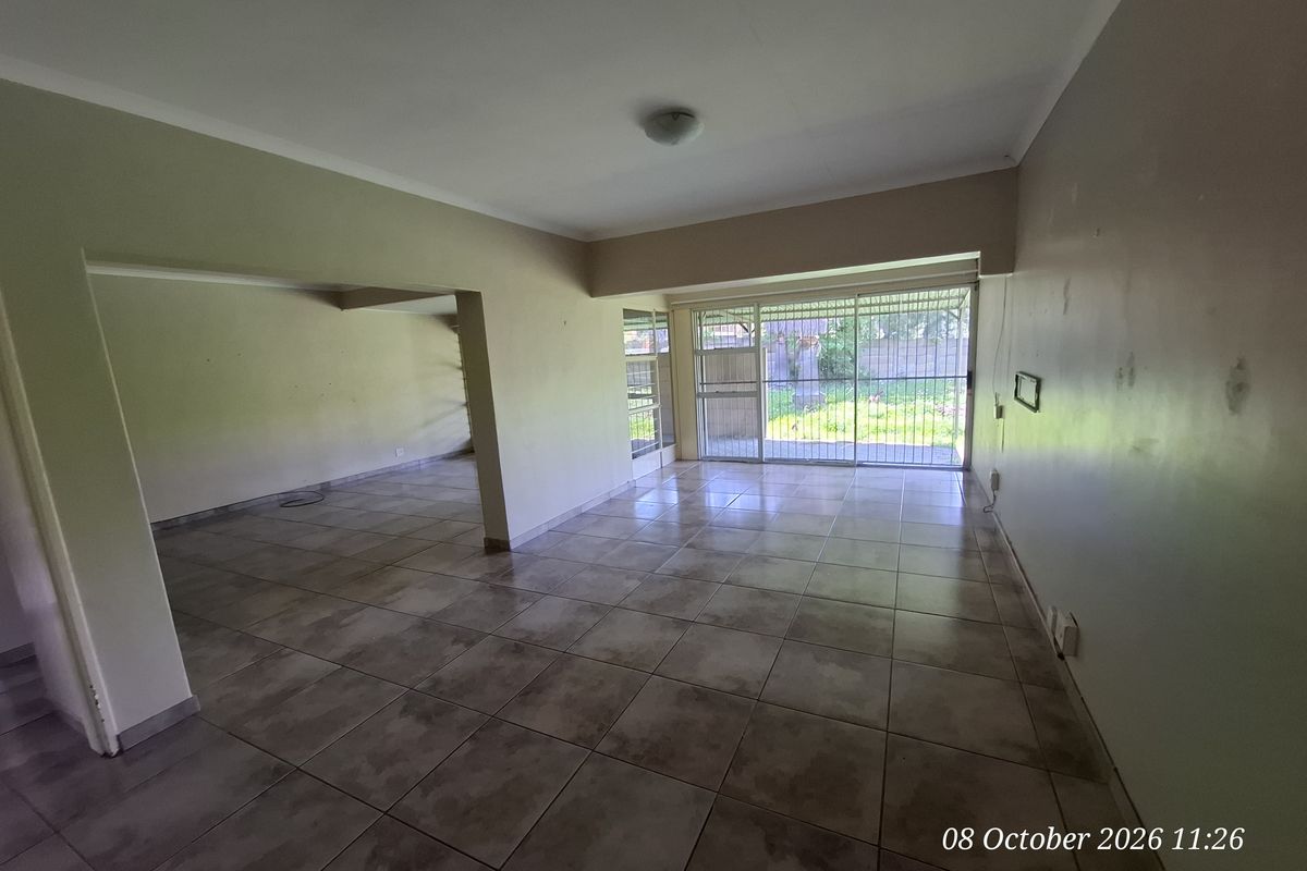 Spacious, empty living area featuring ceramic floor tiles, neutral walls, and a sliding glass door with security gate leading to the rear garden.