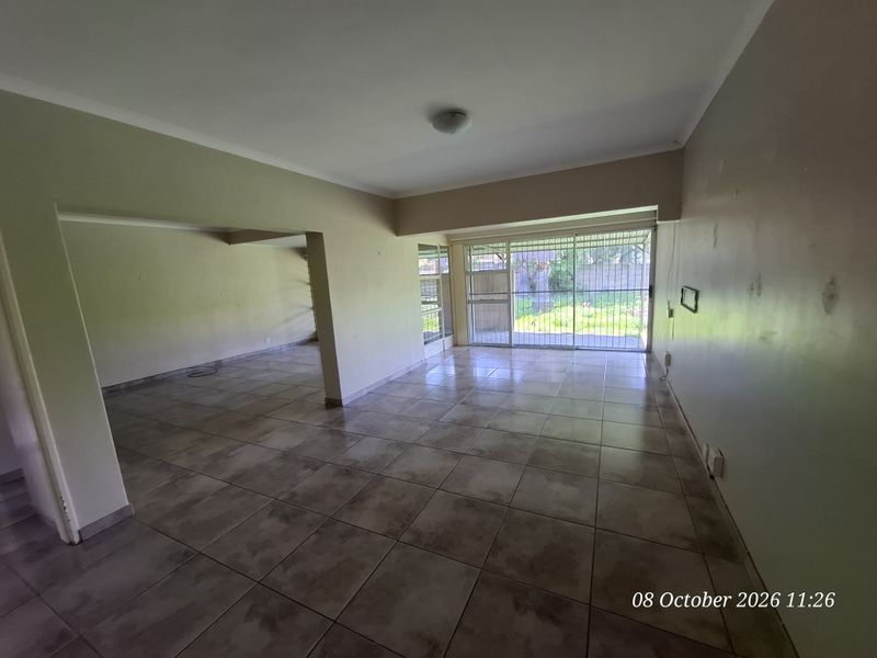 Spacious, empty living area featuring ceramic floor tiles, neutral walls, and a sliding glass door with security gate leading to the rear garden.