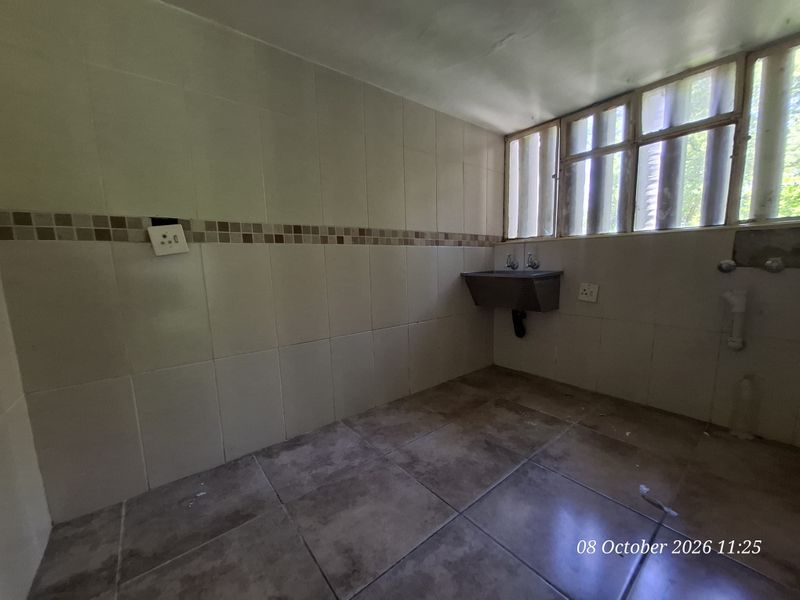 A functional laundry area featuring tiled walls and flooring, a wall-mounted sink, and dedicated plumbing connections for appliances.