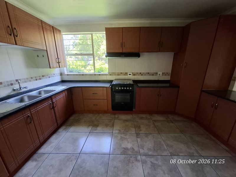 A functional kitchen featuring wooden cabinetry, granite countertops, a double basin sink, and a freestanding stove with an extractor fan.