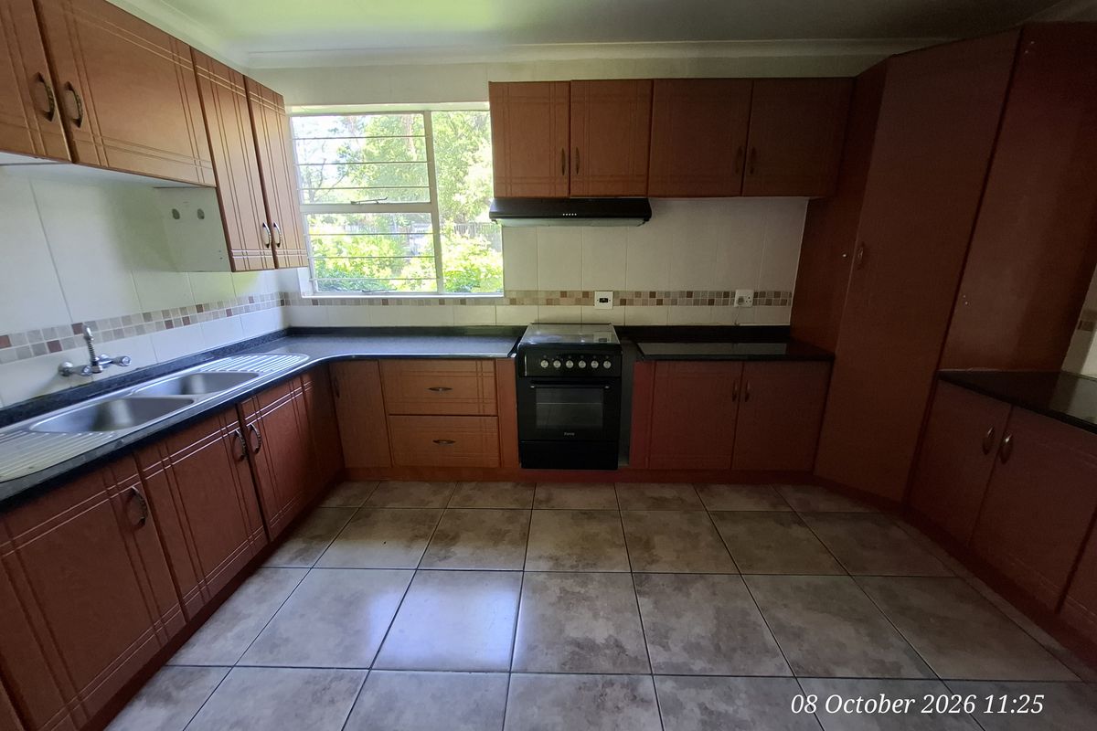 A functional kitchen featuring wooden cabinetry, granite countertops, a double basin sink, and a freestanding stove with an extractor fan.