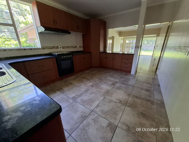 A functional kitchen featuring wooden cabinetry, granite countertops, a freestanding stove with extractor fan, and tiled flooring, offering a clean and practical workspace.