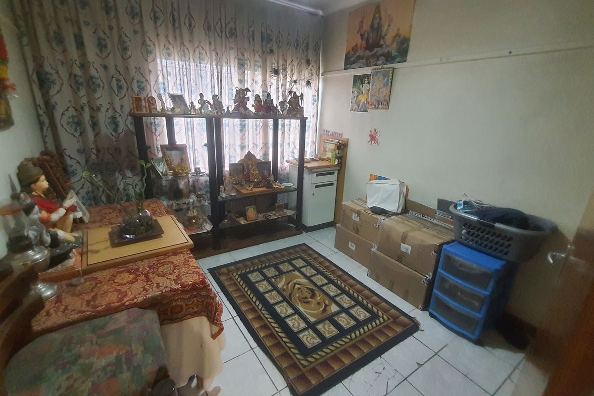 A multi-purpose room featuring tiled flooring and large window with curtains, currently utilized as a prayer and storage space.