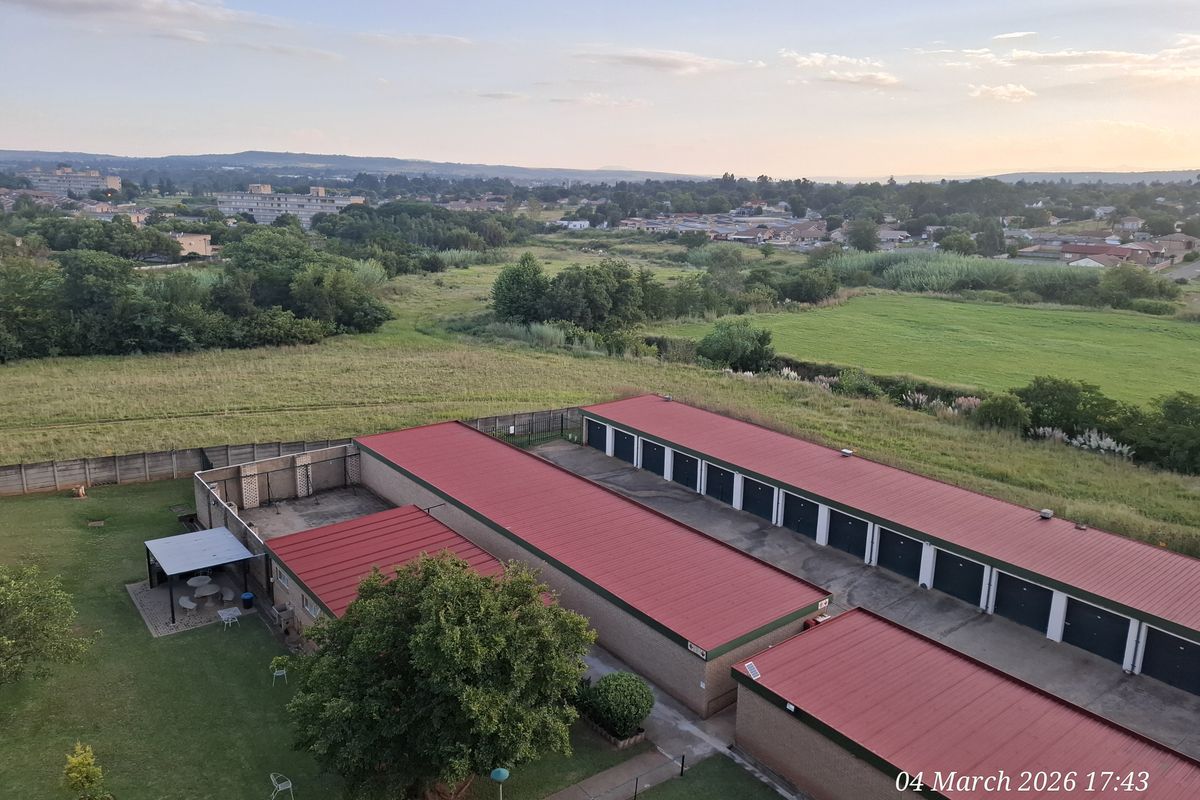 An elevated aerial view of the property grounds, featuring a row of garage units with red metal roofing and surrounding landscaped garden areas.