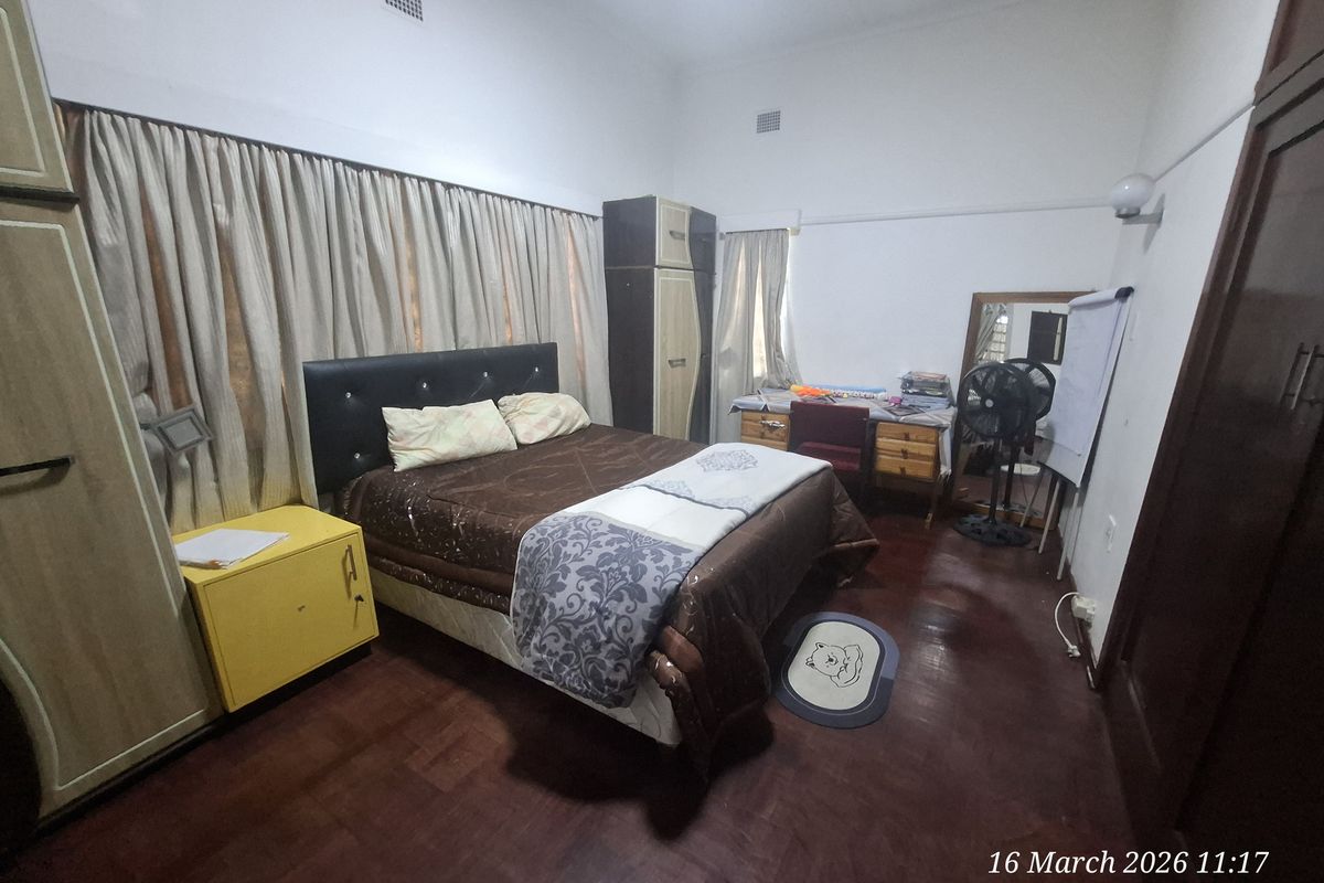 A spacious bedroom featuring dark wood flooring, built-in cabinetry, and high ceilings with integrated ventilation.