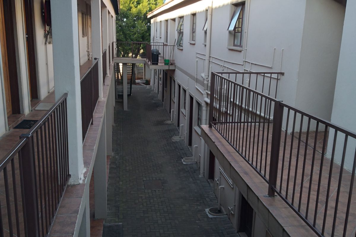 An exterior view of an apartment complex walkway featuring paved ground, metal railings, and multiple unit entrances along the corridor.