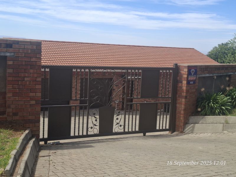 A secure townhouse entrance featuring a brick boundary wall, terracotta tiled roof, and a decorative metal sliding gate.
