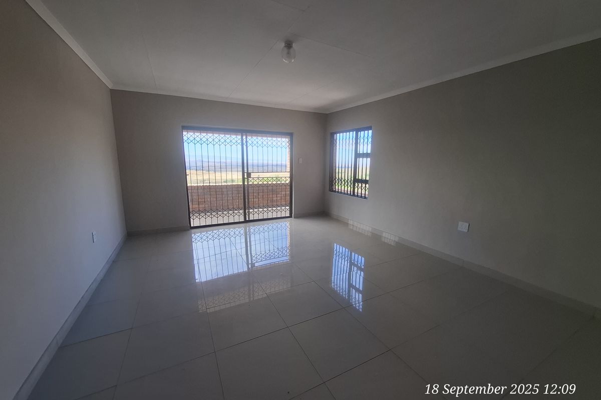 A spacious, empty living area featuring neutral tiled flooring, large sliding glass doors with security gates, and natural light.