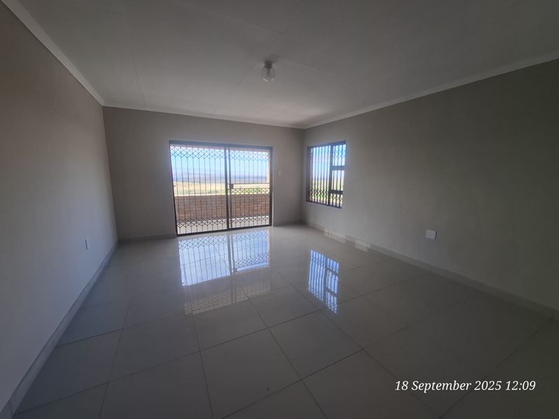 A spacious, empty living area featuring neutral tiled flooring, large sliding glass doors with security gates, and natural light.