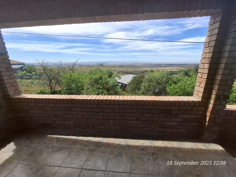 A covered brick patio featuring tiled flooring and an open-air design, offering expansive views of the surrounding landscape.