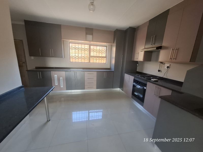 Modern kitchen featuring two-tone built-in cabinetry, stone countertops, integrated oven, hob, and extractor fan with polished tiled flooring.