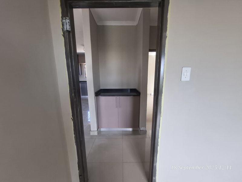 A compact scullery or utility area featuring built-in cabinetry with a stone countertop and neutral tiled flooring, viewed through a doorway.