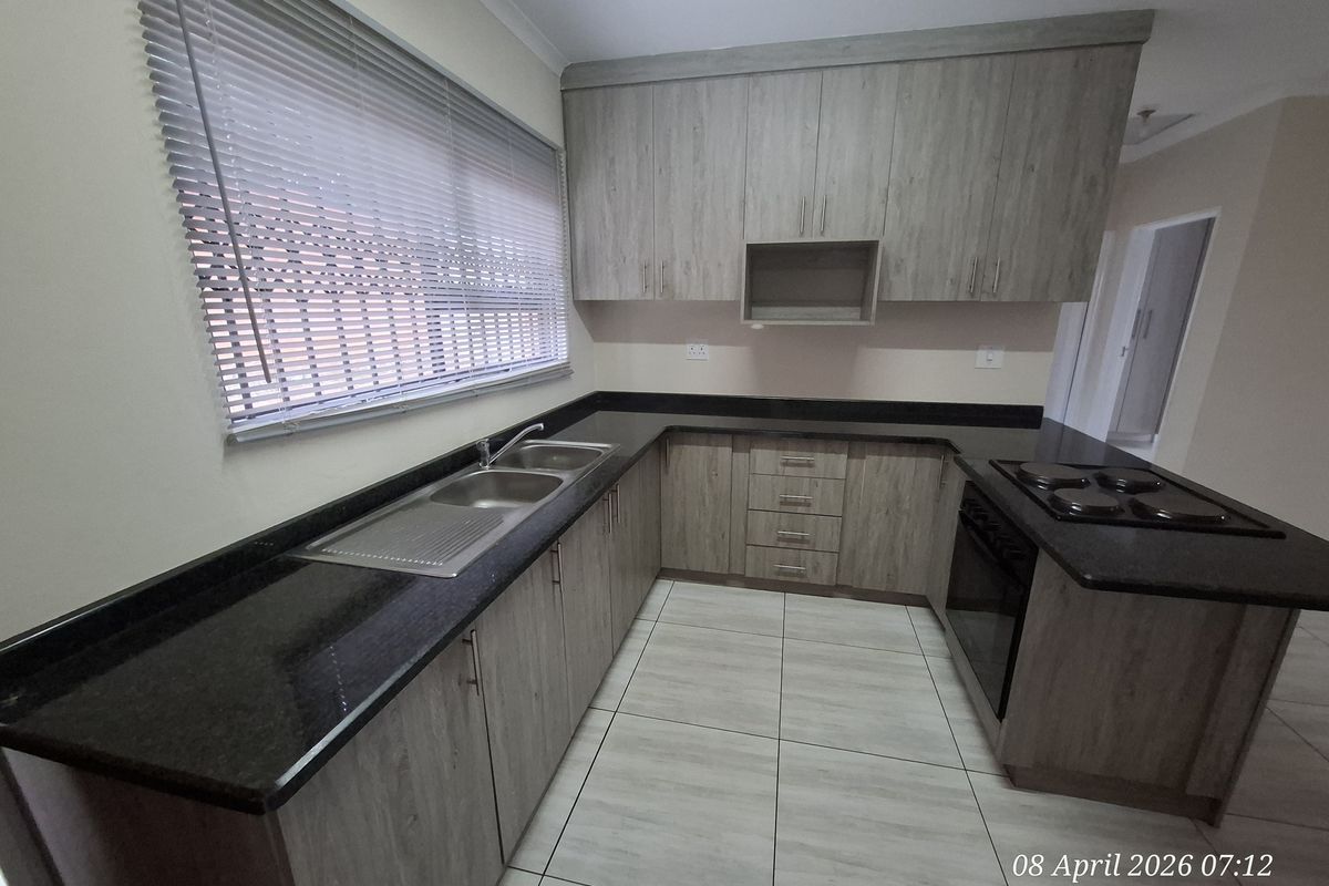 A modern kitchen featuring wood-grain cabinetry, dark granite countertops, a double-basin stainless steel sink, and a built-in electric hob and oven.