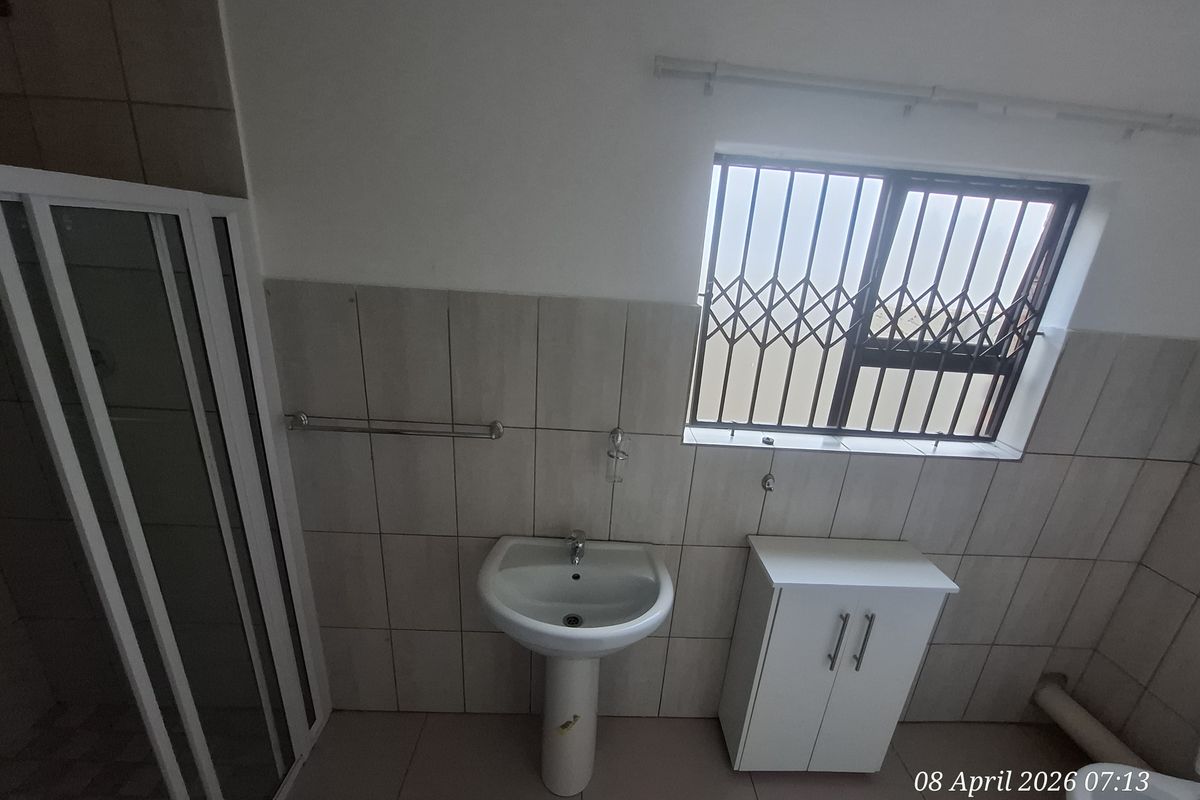 A functional bathroom featuring a pedestal basin, a shower enclosure with a glass door, and a window fitted with security bars.