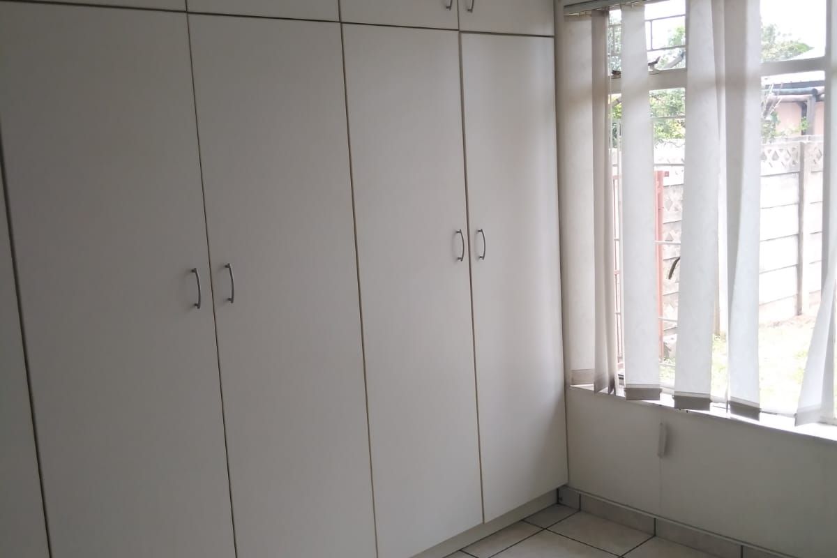 A bedroom featuring floor-to-ceiling built-in cupboards and tiled flooring, providing ample storage space and natural light.