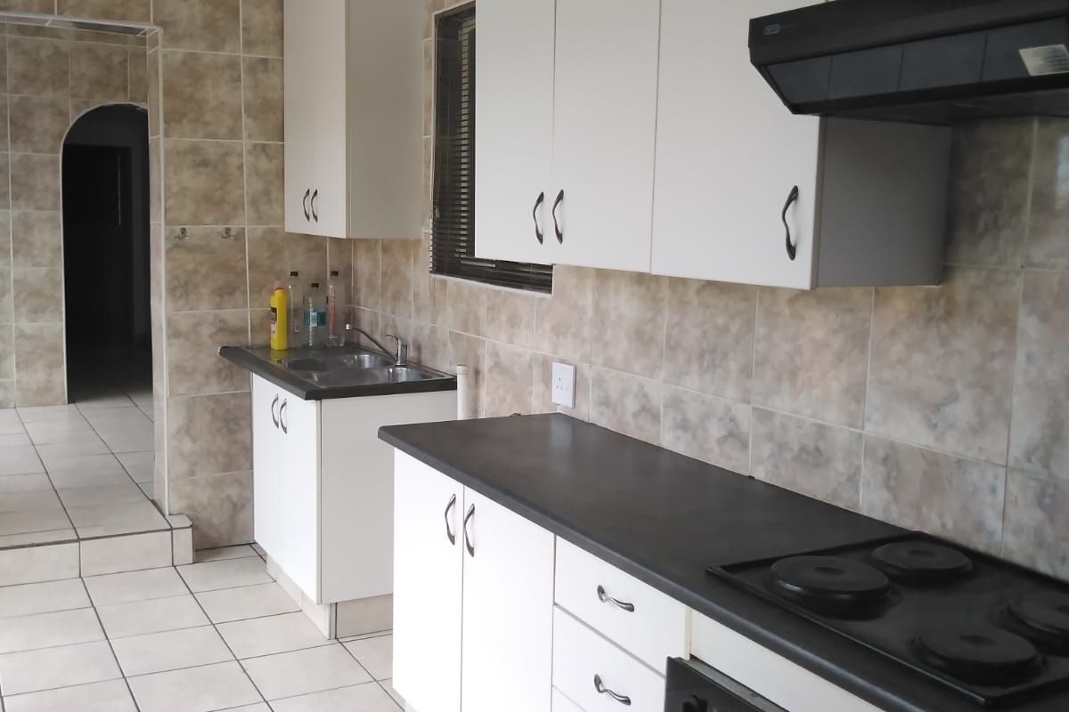 A functional kitchen featuring white cabinetry, dark countertops, a built-in oven with hob, extractor fan, and tiled splashbacks.