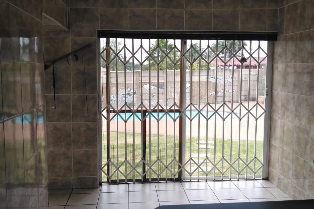 Interior space featuring floor-to-ceiling wall tiles, tiled flooring, and a sliding glass door secured with a metal security gate leading to the pool area.