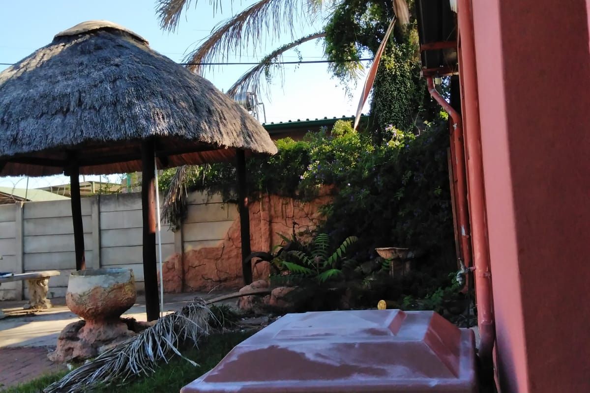 A rear garden area featuring a thatched lapa structure, perimeter walling, and a plastic water storage tank adjacent to the main building.