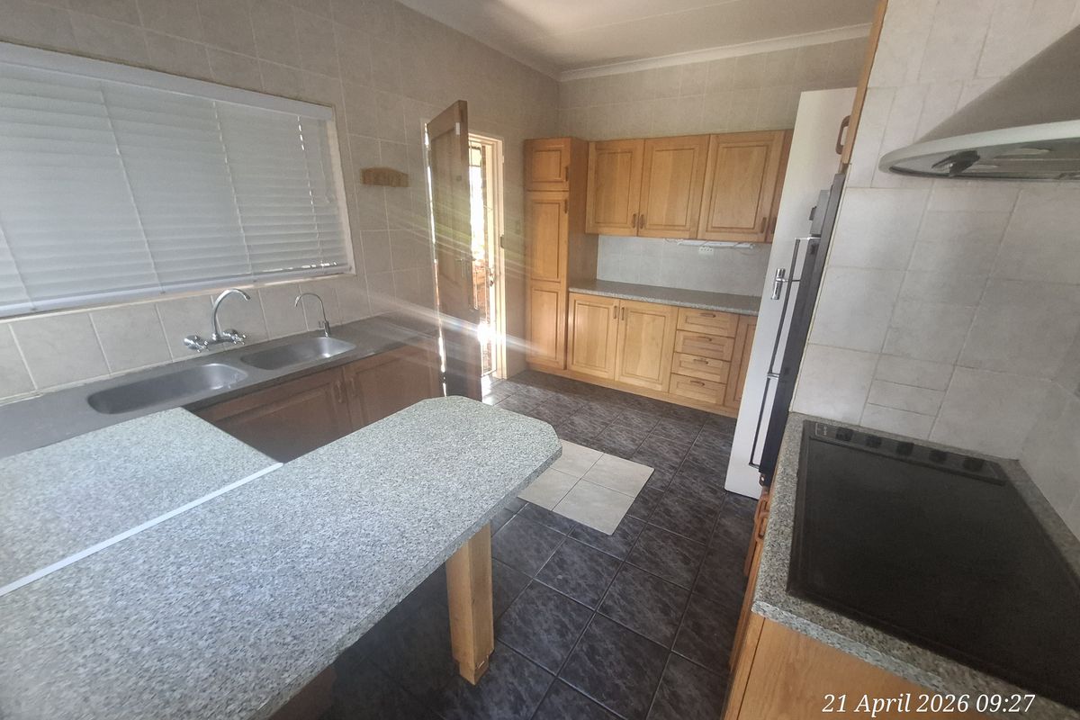 Functional kitchen featuring wooden cabinetry, granite-look countertops, double basin sink, built-in hob, and extractor fan with tiled flooring and backsplash.
