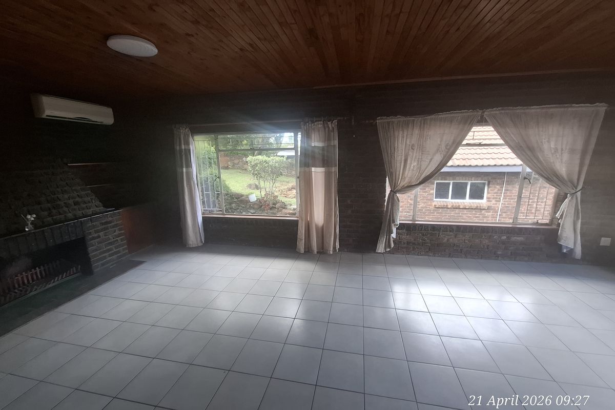 Spacious living area featuring tiled flooring, a built-in brick fireplace, timber-clad ceiling, and large windows providing natural light.