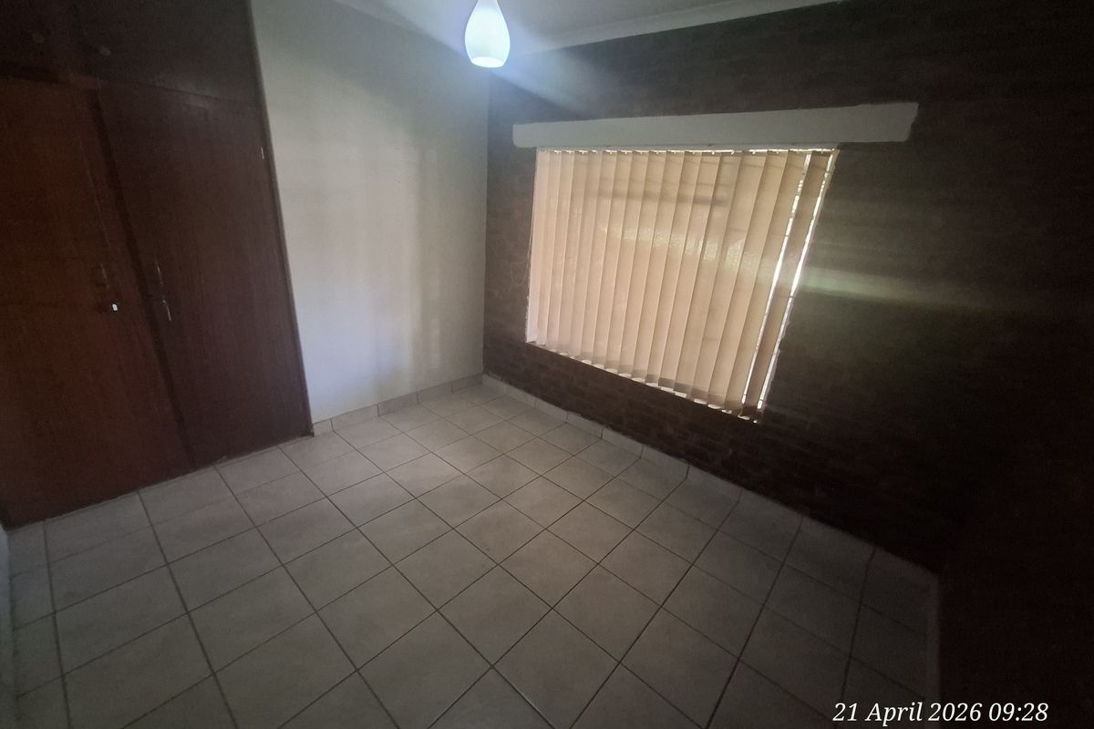 A vacant bedroom featuring tiled flooring, built-in wooden cupboards, and a window with vertical blinds.