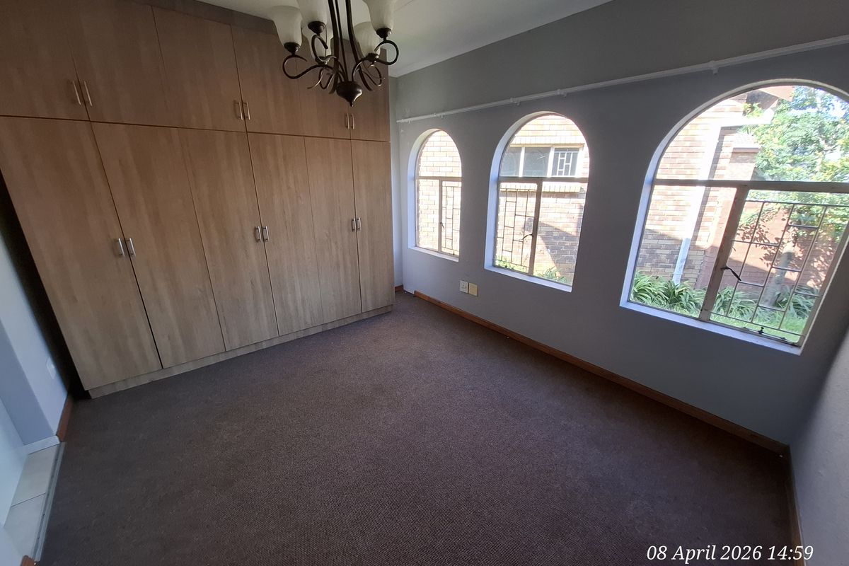 A bedroom featuring built-in wooden cupboards, carpeted flooring, and three distinctive arched windows providing natural light.
