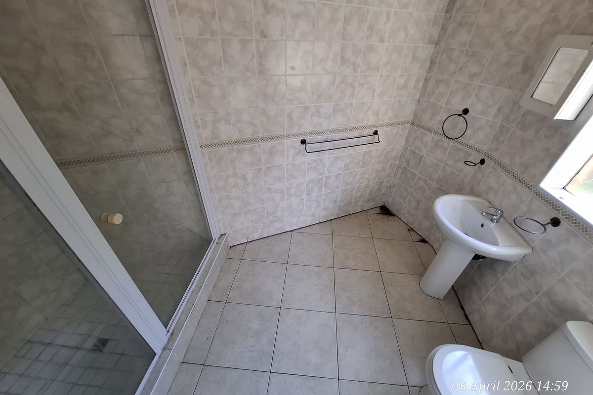A dated bathroom featuring a pedestal basin, toilet, and a glass-enclosed shower with tiled walls and flooring.