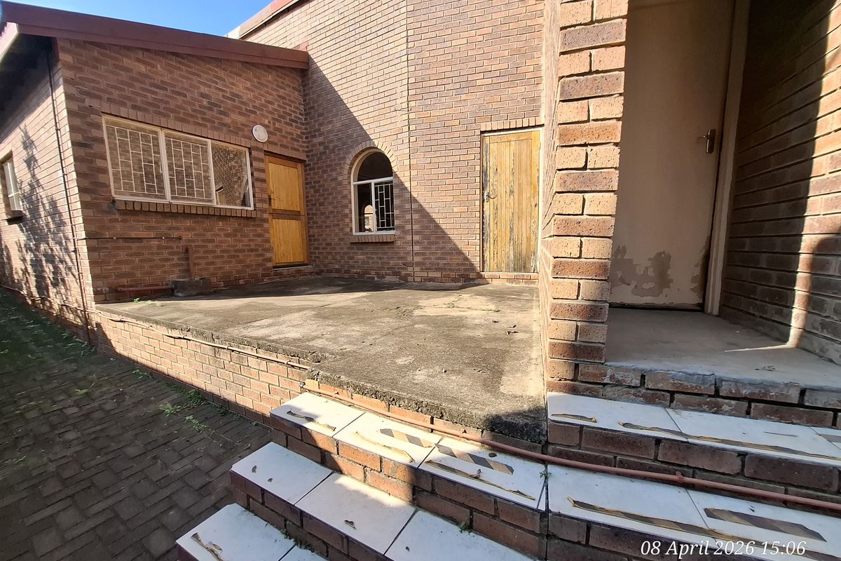 A rear exterior view of a brick townhouse featuring a concrete patio area, tiled steps, and multiple access doors.