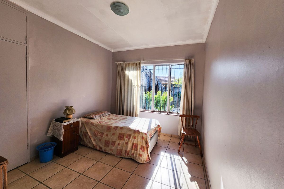 A bedroom featuring tiled flooring, a built-in cupboard, and a window fitted with security bars, offering natural light.