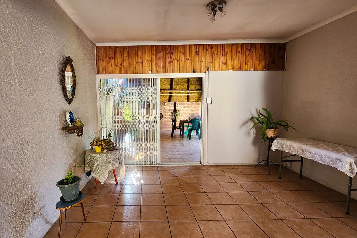 A spacious living area featuring tiled flooring and a sliding door with security gate leading to an outdoor patio.