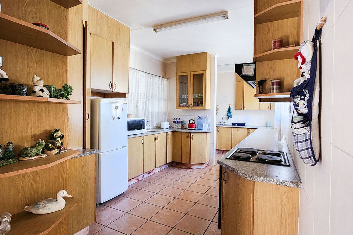 A functional kitchen featuring wood-laminate cabinetry, built-in electric hob, tiled flooring, and ample storage space with a practical layout.