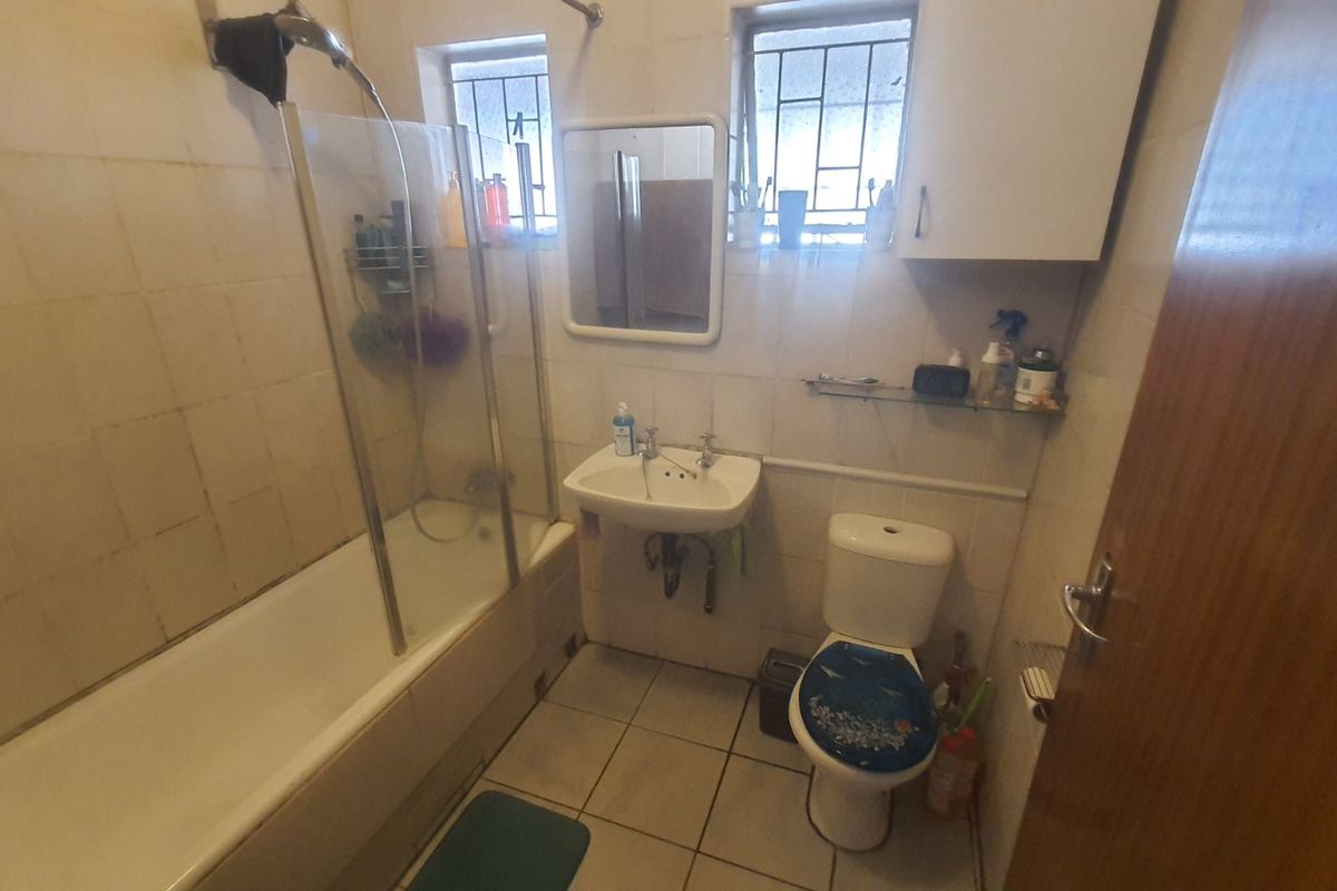 A compact bathroom featuring a bathtub with a glass shower screen, a wall-mounted basin, and a standard toilet with tiled walls and flooring.