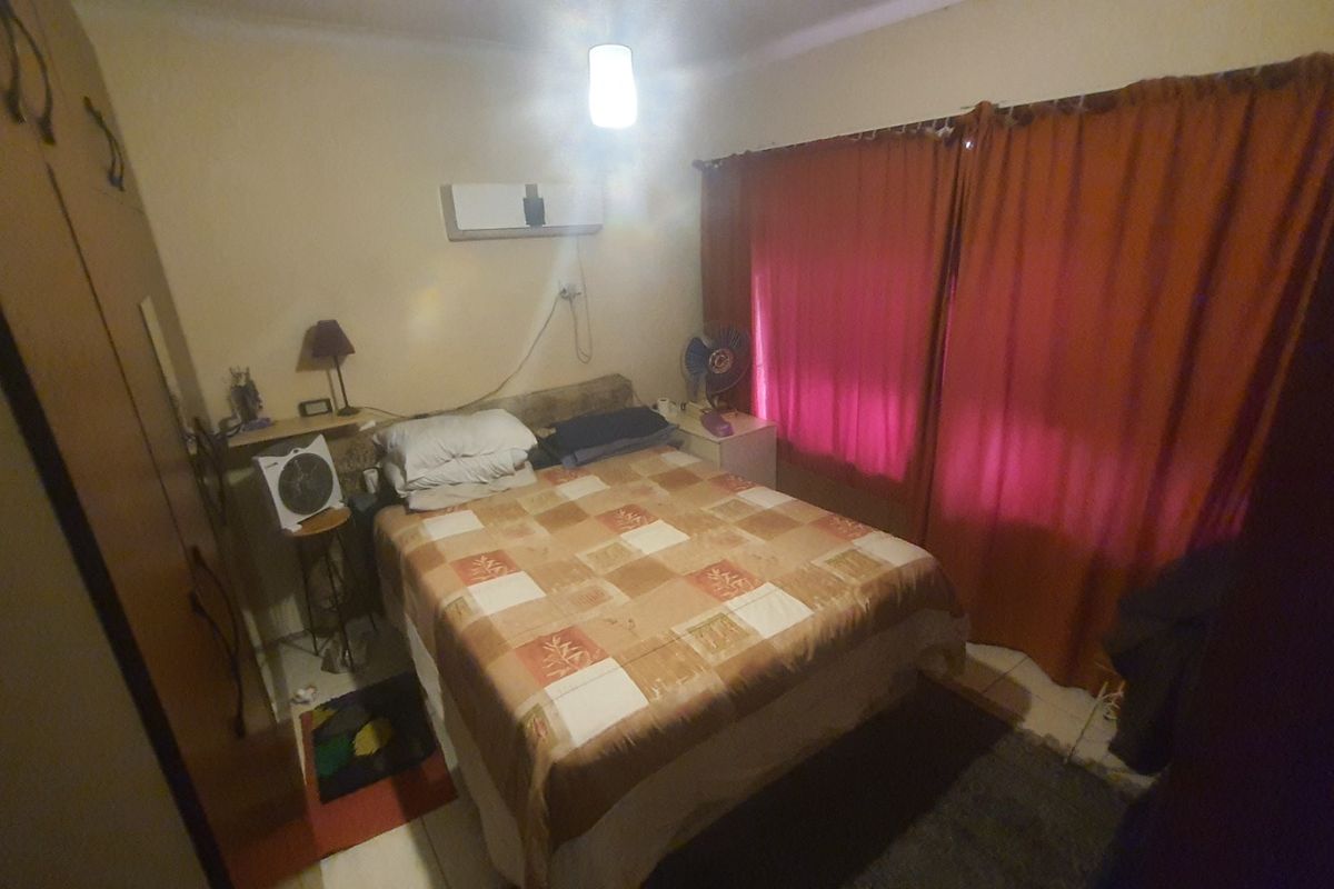 A bedroom featuring built-in cabinetry, a wall-mounted air conditioning unit, and large windows covered by curtains.