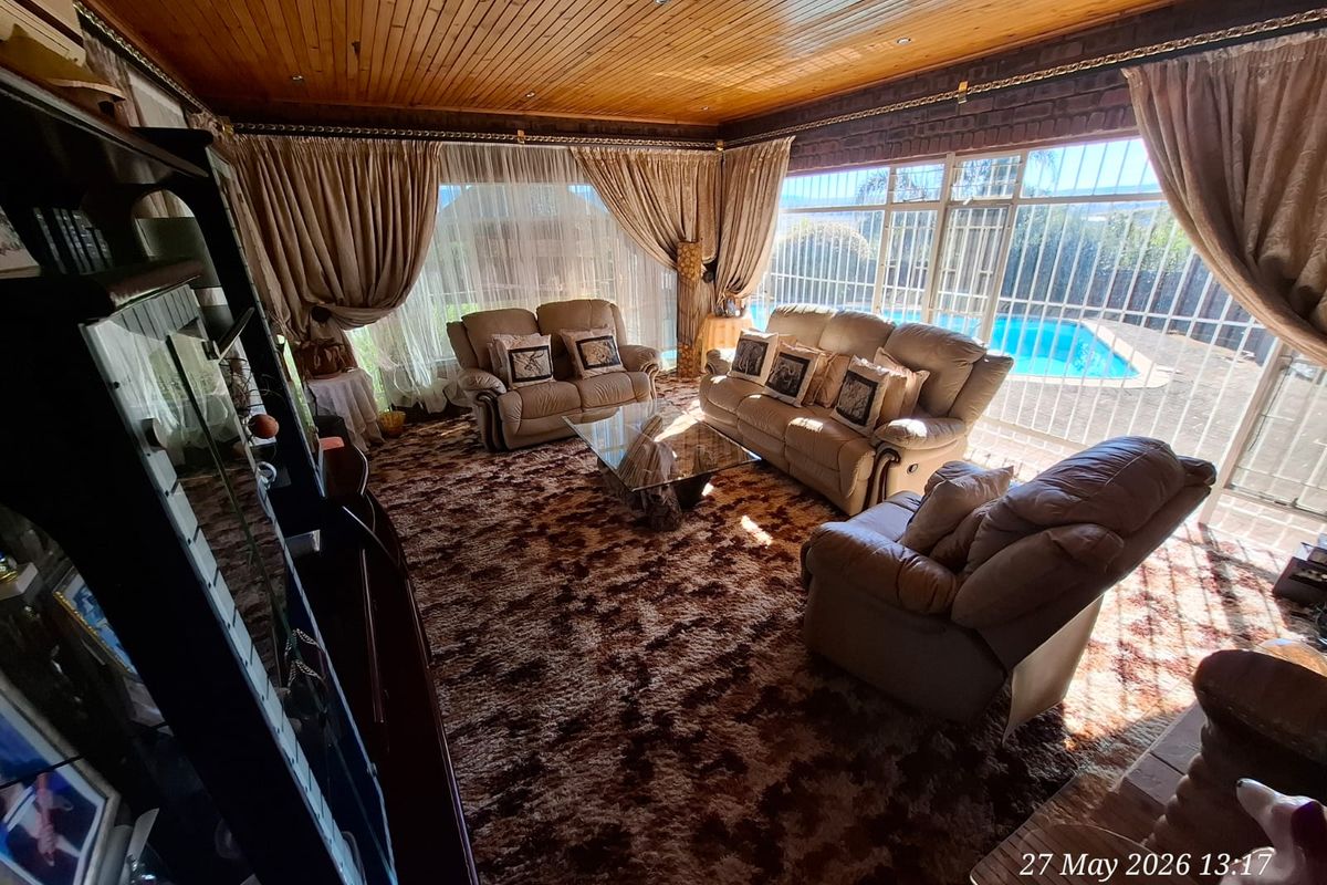 Spacious living room featuring a wood-paneled ceiling, exposed brick walls, and large windows with direct views of the outdoor pool area.