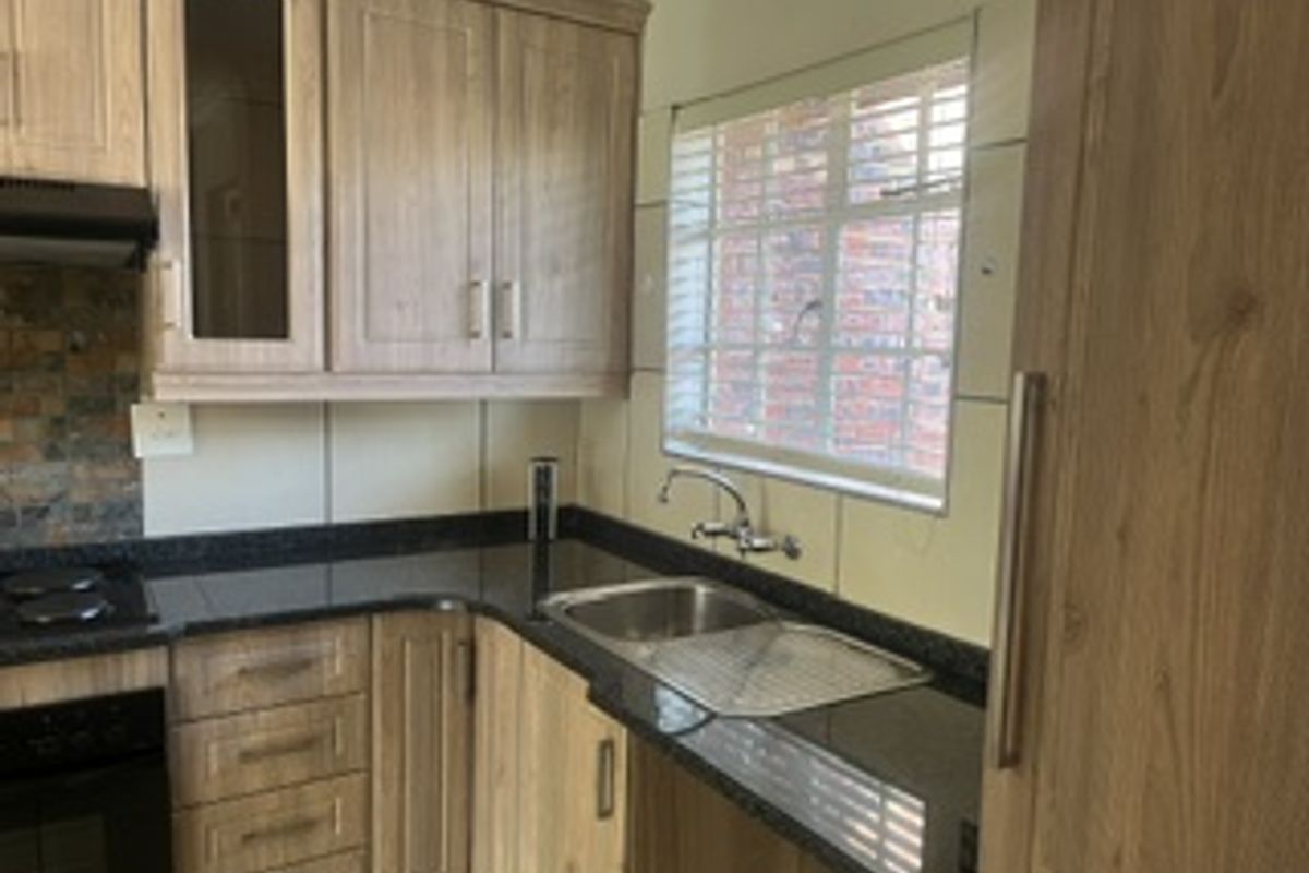 Functional kitchen featuring light wood-grain cabinetry, dark stone-look countertops, stainless steel sink, and integrated oven with hob.