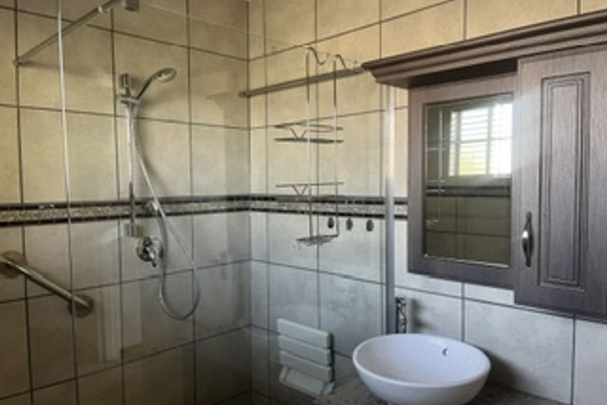 A functional bathroom featuring a glass-enclosed shower with a grab rail, a vanity with a vessel sink, and wall-mounted cabinetry.