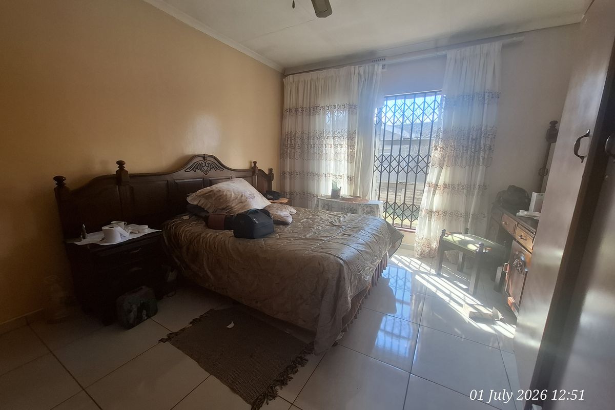 A bedroom featuring tiled flooring, a ceiling fan, and a window fitted with a security gate.