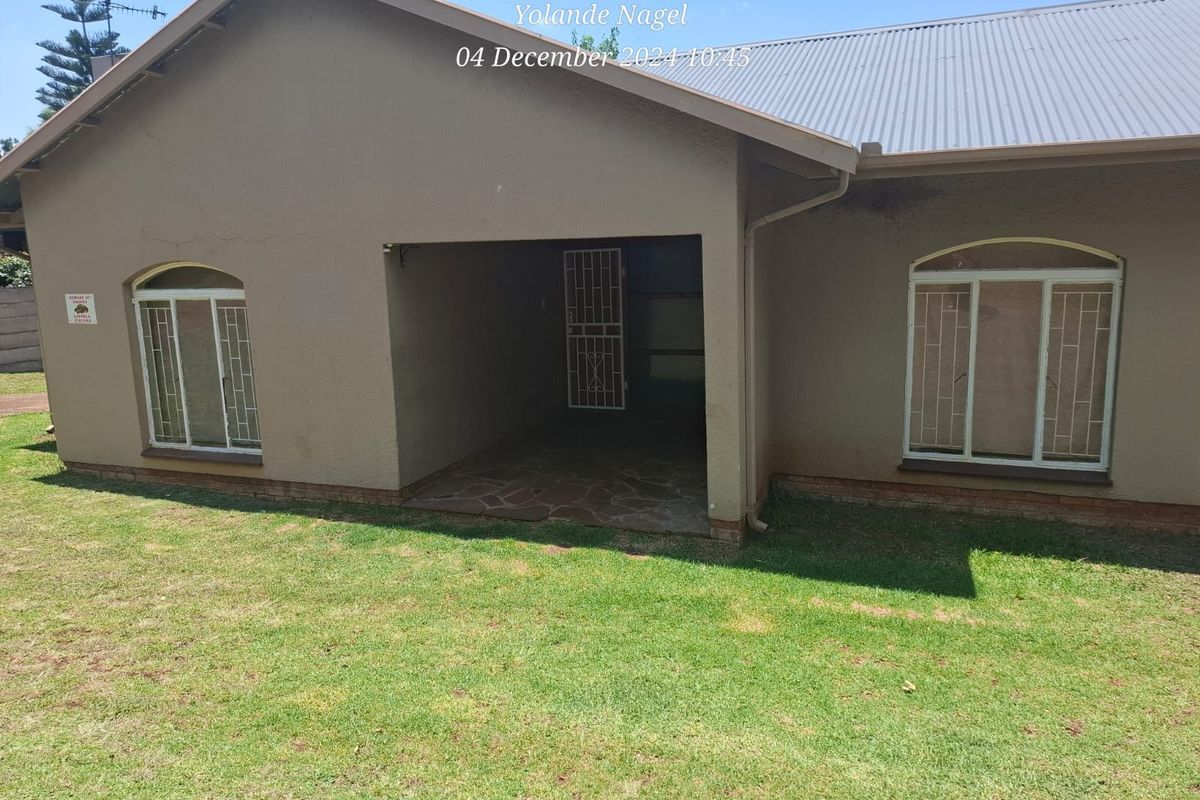 Rear view of the house featuring a covered patio area, corrugated metal roofing, and security bars on the windows.