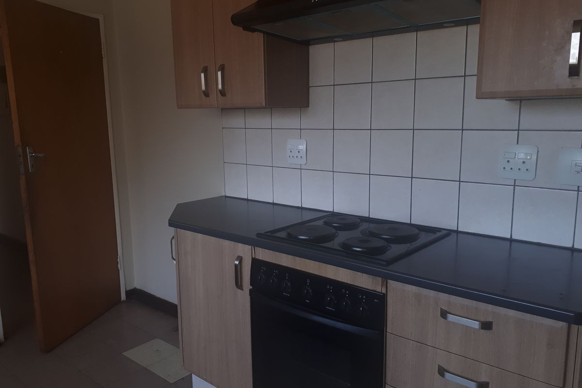 A functional kitchen featuring laminate cabinetry, dark countertops, a built-in oven with hob, and a tiled splashback.