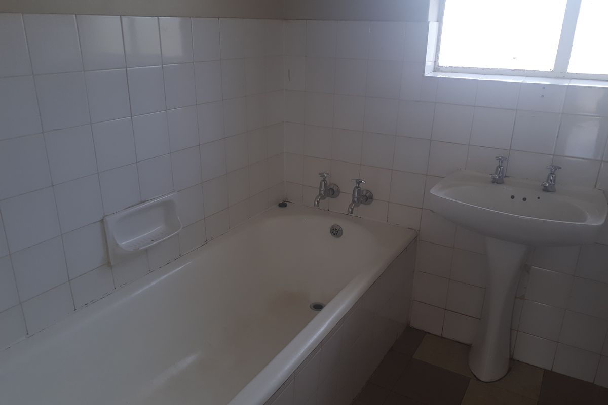A dated bathroom featuring a standard bathtub and pedestal basin with white wall tiling and tiled flooring.