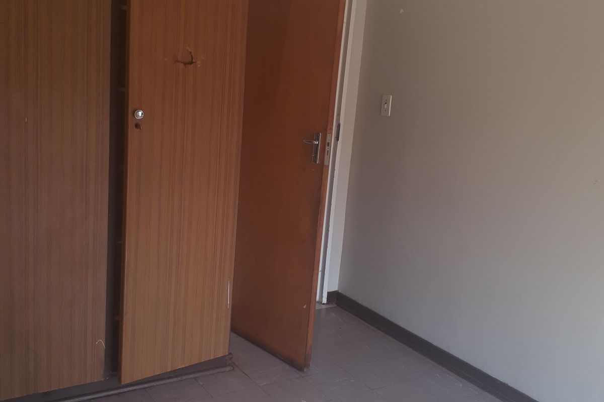 An empty bedroom featuring tiled flooring and built-in wooden cupboards, requiring minor cosmetic updates to the walls and cabinetry.