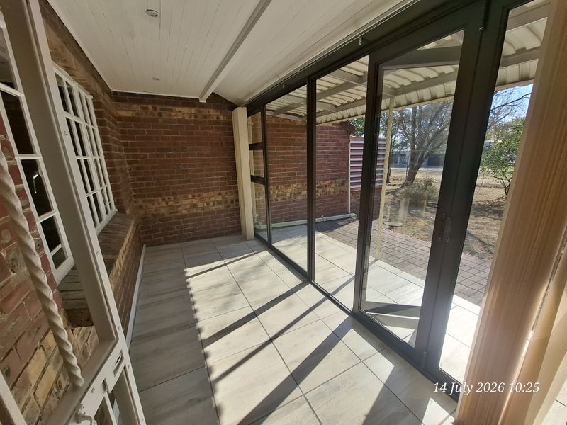 A covered patio area featuring exposed brick walls, modern timber-look floor tiles, and large aluminium sliding doors providing access to the garden.