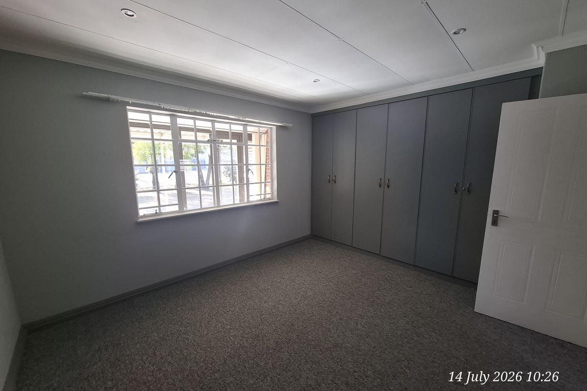 A clean, empty bedroom featuring neutral grey walls, carpeted flooring, and extensive built-in storage cupboards.