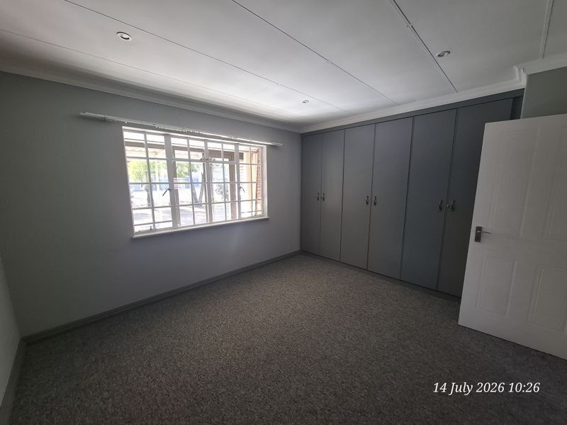 A clean, empty bedroom featuring neutral grey walls, carpeted flooring, and extensive built-in storage cupboards.