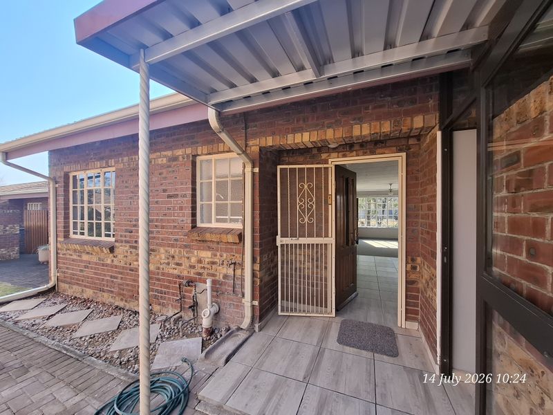 Rear exterior view of a face brick retirement unit featuring a covered patio area, security gate, and tiled flooring.