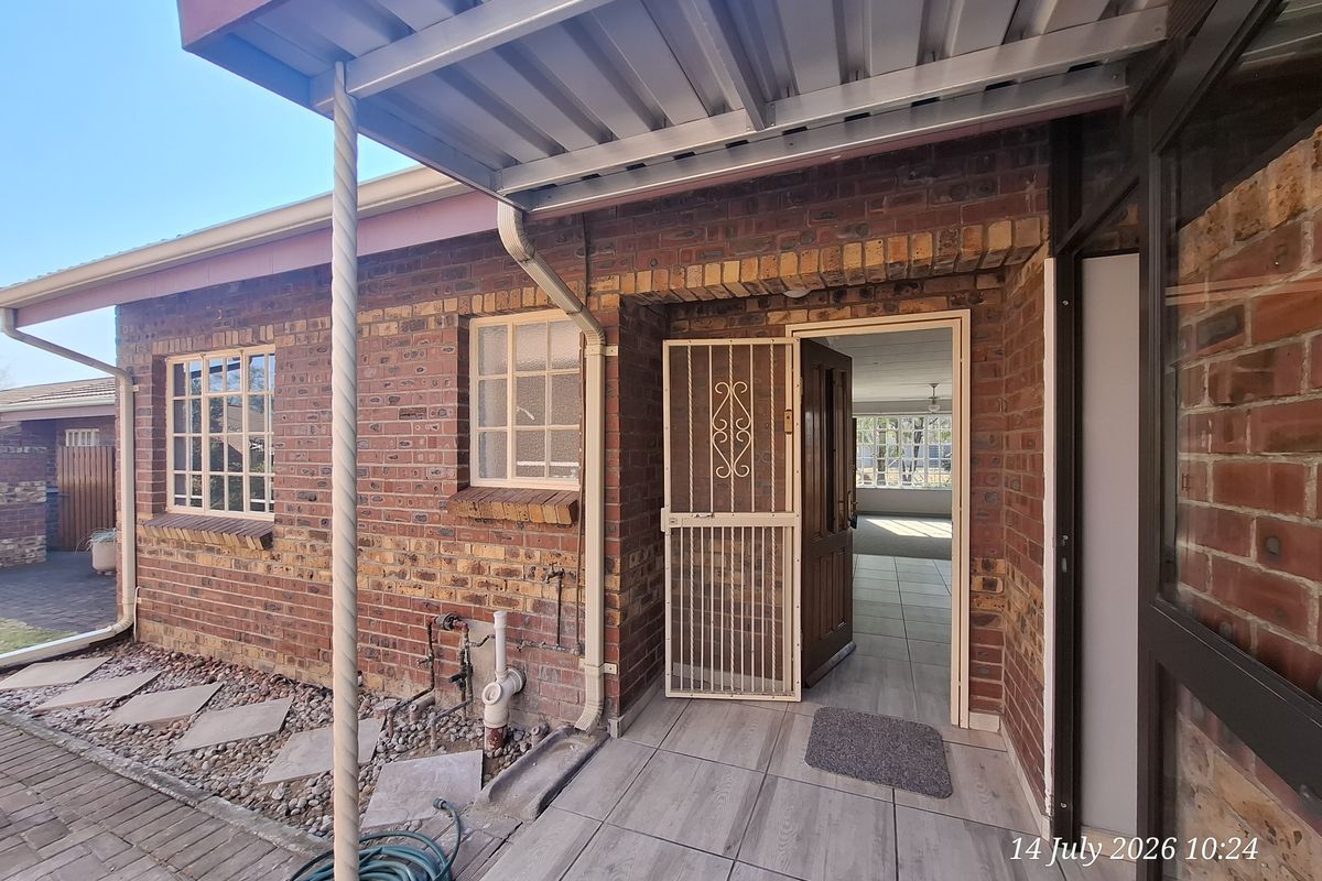 Rear exterior view of a face brick retirement unit featuring a covered patio area, security gate, and tiled flooring.