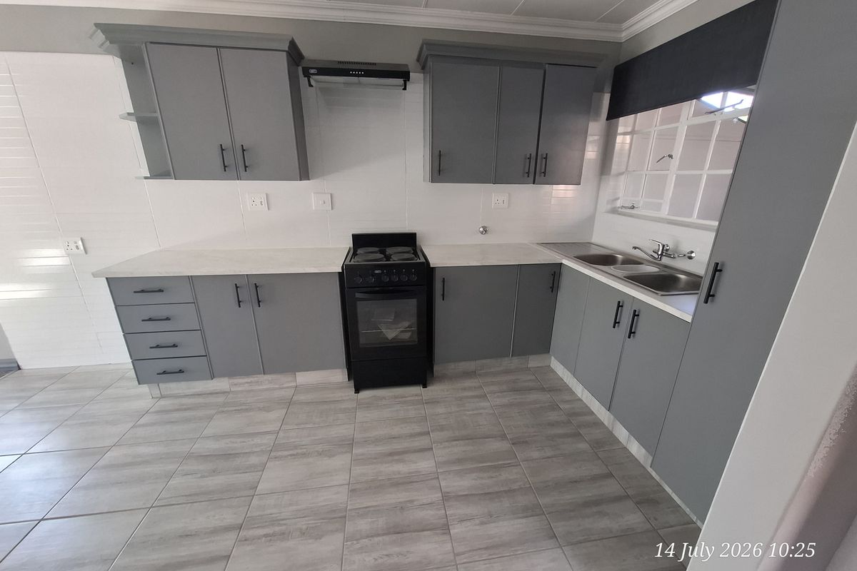 A clean, modern kitchen featuring grey cabinetry, laminate countertops, a freestanding stove with extractor fan, and a double bowl sink with tiled splashback.