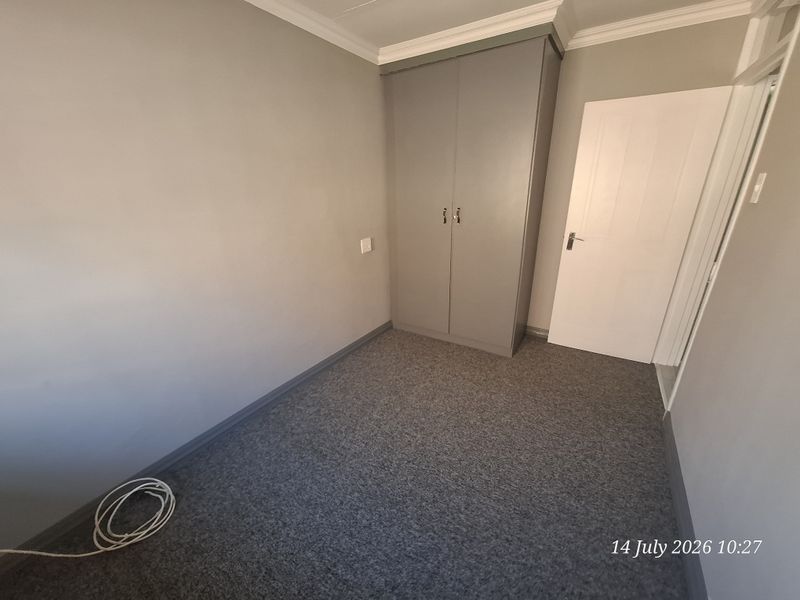 A clean, empty bedroom featuring neutral grey walls, grey carpet flooring, and a built-in wardrobe with white door trim.