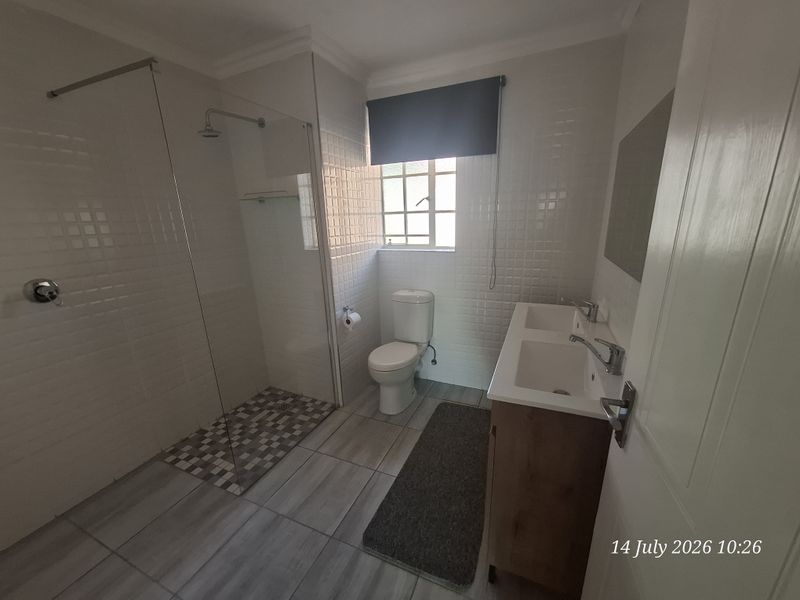 A modern, well-maintained bathroom featuring a spacious walk-in shower with glass screen, a double vanity unit, and neutral tiled finishes throughout.