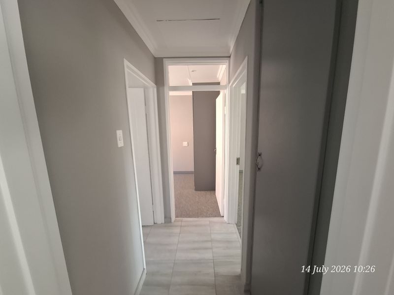 A clean, neutral-toned hallway featuring tiled flooring, a built-in storage cupboard, and a transom window providing natural light to the adjacent room.